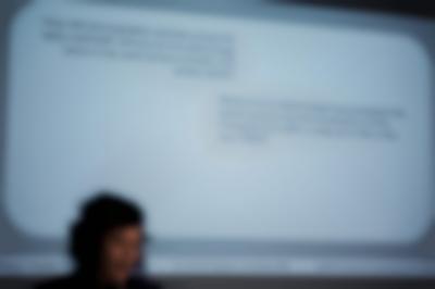 Megan's head appears in front of the powerpoint slide projection. The slide asks two questions about how the usage of photography and video throughout the twentieth century.