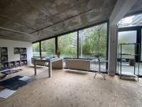 Workspace with large windows. There is a desk, a shelf, a smaller round table and large sheets of paper or photographic print on the floor. On the wall, hang several photographic prints showing the same flower.