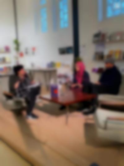 Megan Hoetger, Arwa Aburawa and Turab Shah sit around a low table having a discussion. Megan and Arwa are holding microphones. There is a book propped up on the table.