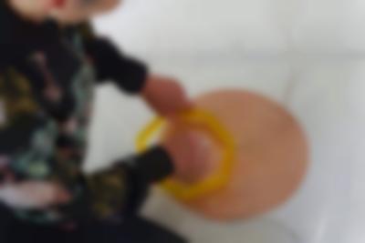 A coil spiral has been stuck to a white floor with a transparent plastic. There are two cables attached to it, one to the centre and the other to the edge. A person can partially be seen sitting next to it. With their left hand they are holding a small yellow heptagon structure against the spiral. With their right hand, they are touching the spiral through the middle of the structure.