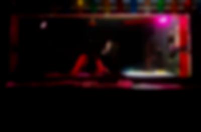 A person stands in a dark DJ booth, adjusting the knobs on a DJ deck. To their right, a bright light shines upwards from a light box set next to the deck.