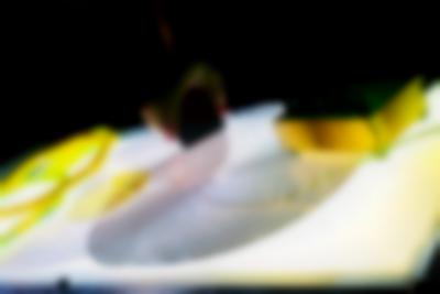 On top of a light box surface, there are two coil spirals and a small sound deck with knobs. A hand can be seen holding an object, which they've put on top of one of the spirals.