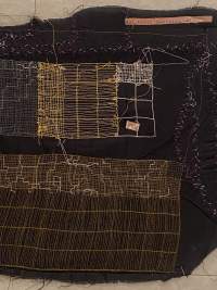 Section of a piece of dark fabric with stitches in white, brown and yellow. These stitches appear in different shapes and form patterns.