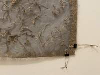 Close up section of a large rectangular piece of fabric hung on the wall. There is some texture to it, created with stitching.