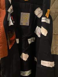 Detail of a thick piece of fabric to which small patches of other fabric have been attached. These patches have drawings or writing on them.